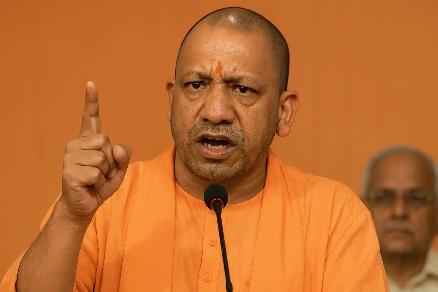 A visual of UP CM Yogi Adityanath speaking at a political rally, with a serious expression.